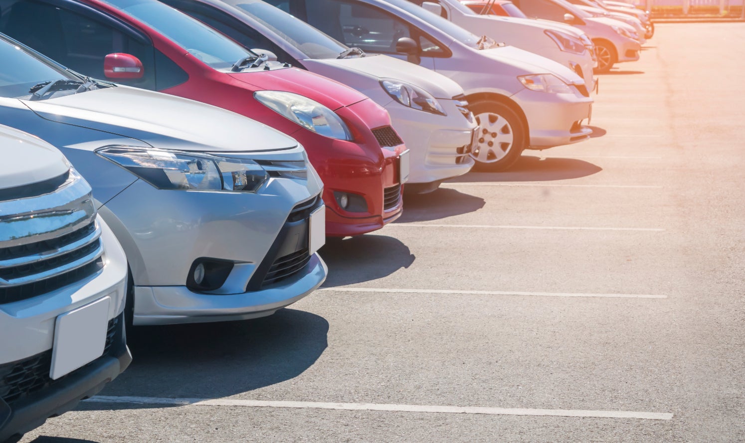 The front part of a series of used cars in a row on a dealership lot.