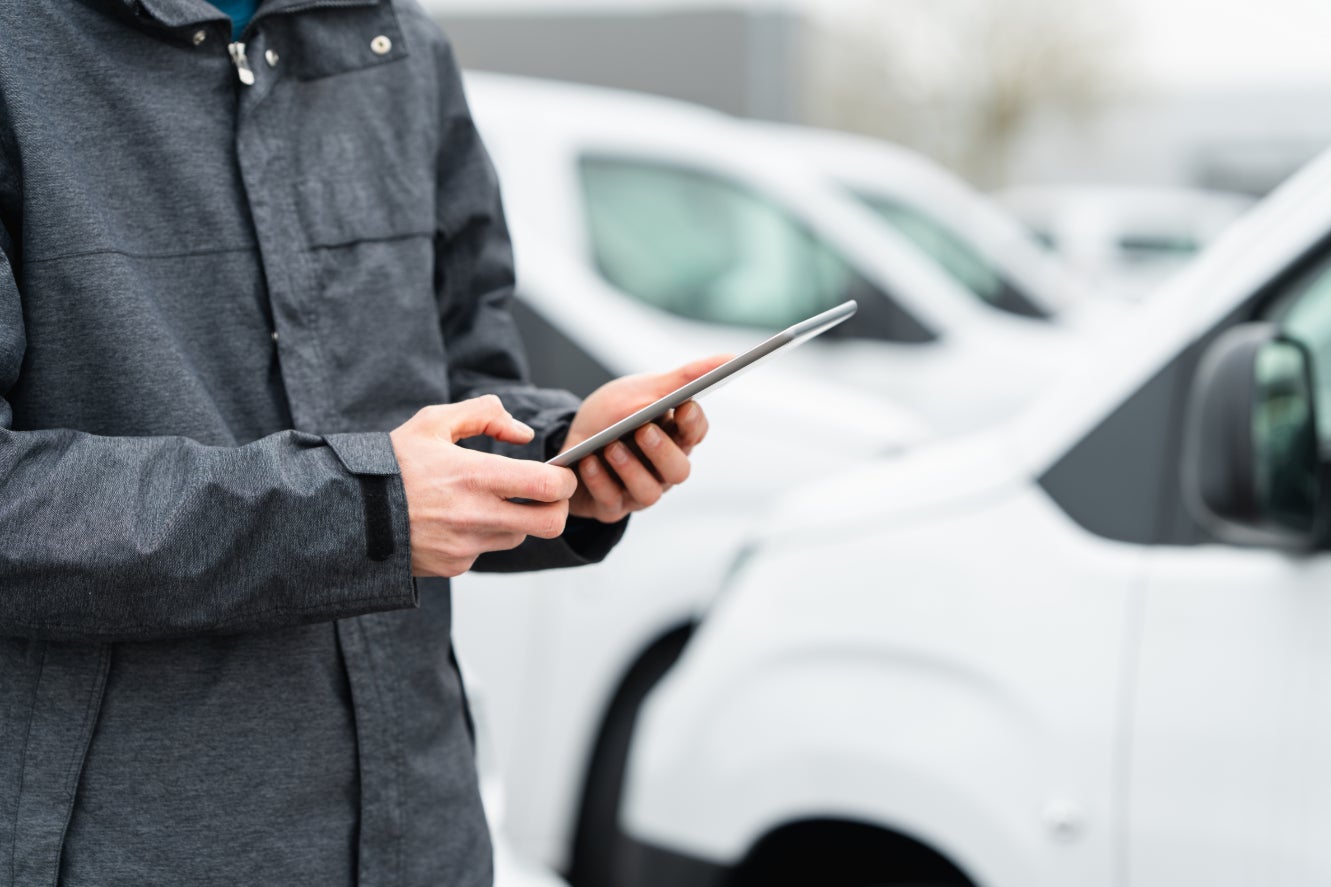 A technician looking at a pad in a vehicle service center near white cars.